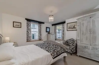 a bedroom with a bed and a dresser and windows at Historic Osborne House very close to the beach in Looe