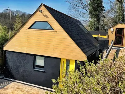 a small house with a gambrel roof and yellow doors at Chy Glynn. Luxury lodge with hot tub and views. in St. Agnes