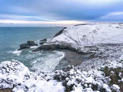 a snow covered cliff with a beach and the ocean at Chy Mena. South facing lodge with hot tub & views. in St. Agnes