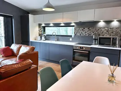 a kitchen with blue cabinets and a couch and a table at Chy Cos. South facing lodge with balcony & views. in St. Agnes