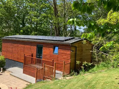 a small wooden cabin with a black roof at Chy Cos. South facing lodge with balcony & views. in St. Agnes