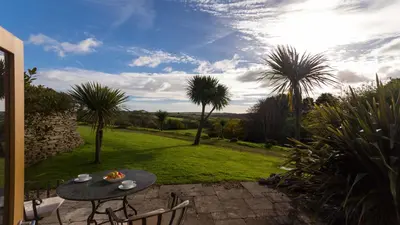 a patio with a table and chairs and palm trees at BADGERS HOLLOW in Fowey