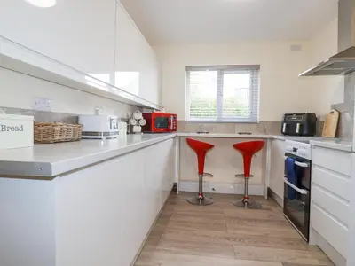 a kitchen with white counters and red stools at Falcon House in Tintagel