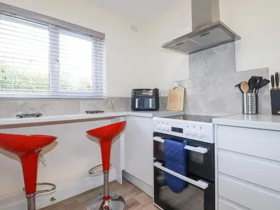 a kitchen with white counters and red stools at Falcon House in Tintagel