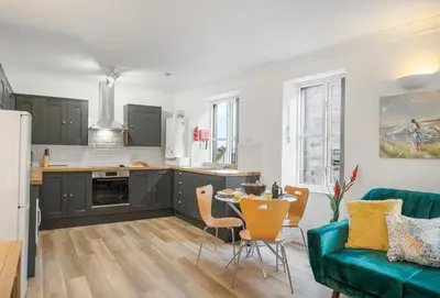 a kitchen and living room with a green couch and a table at Harbour Steps in Falmouth