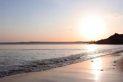 a beach with the sun setting over the water at Sandy cottage, nr Eden & beaches in St Austell