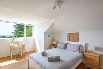 a bedroom with a bed and a table and a window at Manacles - Spacious flat near beach with sea views & parking in Falmouth