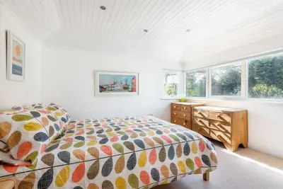 a bedroom with a bed and a dresser and windows at Trevint - Modern beach house in Falmouth near beach, private garden and parking in Falmouth