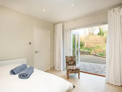 a bedroom with a bed and a chair and a window at The Studio At Granny's Well in Fowey