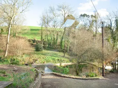 a river in a field with trees and a road at The Studio At Granny's Well in Fowey