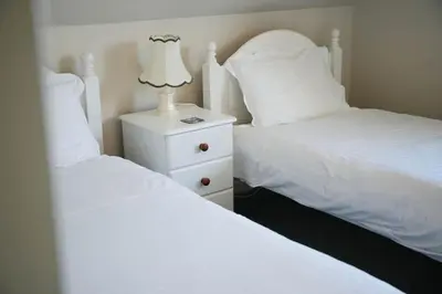 two beds with white sheets and a lamp on a night stand at Haven Cottage, Port Isaac Bay Holidays in Port Isaac