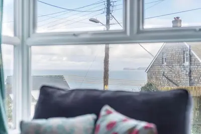a couch in front of a window with a view of the ocean at Tregenna, Port Isaac Bay Holiday in Port Isaac