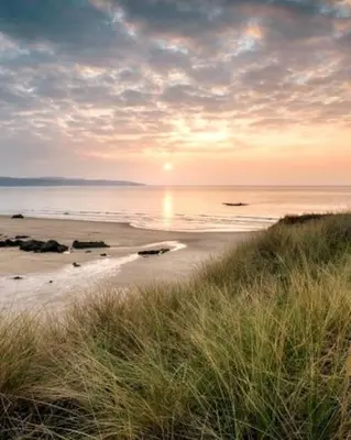 a view of a beach with the sun setting over the water at Family friendly home by the beach in Hayle
