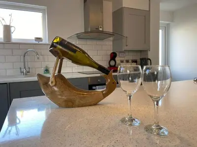 a bottle of wine in a wooden basket next to two wine glasses at The Emslie Road Beach Flat in Falmouth