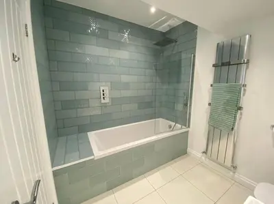 a bathroom with a tub and a shower with blue tiles at The Emslie Road Beach Flat in Falmouth