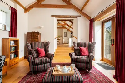a living room with two chairs and a table at Linhay at East Trenean Farm -Luxury retreat for 2 with stunning rural views, private hot tub and EV charging in Looe