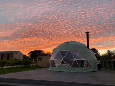 a tent on a deck with a sunset in the background at Glamping Dome Elysian Fields in Helston