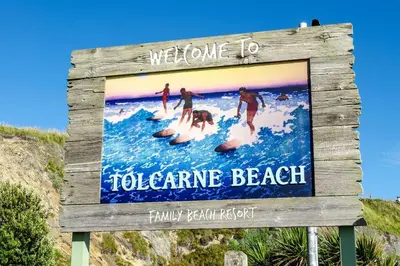 a sign at the beach with people surfing on the waves at Luxury 3 floor Town House by Tolcarne Beach in Newquay
