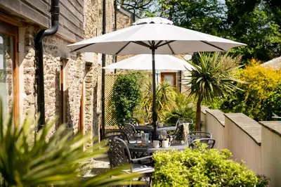 a table with an umbrella in a garden at Corn Barn at East Trenean Farm -Luxury Cornish Barn Conversion sleeping 8 with hot tub, private garden, rural views and EV facilities in Looe