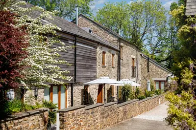 a brick building with an umbrella in front of it at Corn Barn at East Trenean Farm -Luxury Cornish Barn Conversion sleeping 8 with hot tub, private garden, rural views and EV facilities in Looe