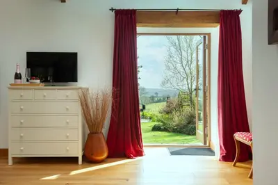 a room with a sliding glass door with red curtains at East Trenean Farm Cottages -4 Luxury Cornish Cottages sleeping 20 with hot tubs, private gardens, rural views and EV facilities in Looe