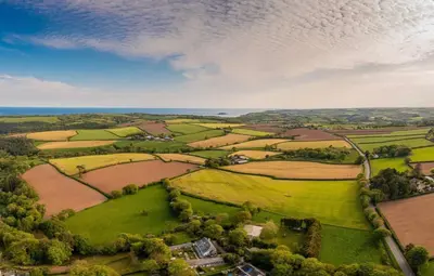 an aerial view of a green field with a house at Threshing Barn at East Trenean Farm -Stunning Cornish Cottage sleeping 6 with hot tub, private garden, rural views and EV facilities in East Looe