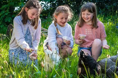 three girls sitting in the grass playing with food at Threshing Barn at East Trenean Farm -Stunning Cornish Cottage sleeping 6 with hot tub, private garden, rural views and EV facilities in East Looe