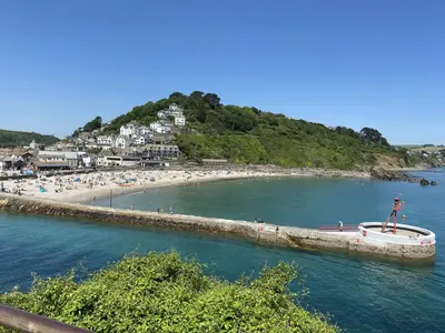a group of people on a beach with a boat in the water at Threshing Barn at East Trenean Farm -Stunning Cornish Cottage sleeping 6 with hot tub, private garden, rural views and EV facilities in East Looe