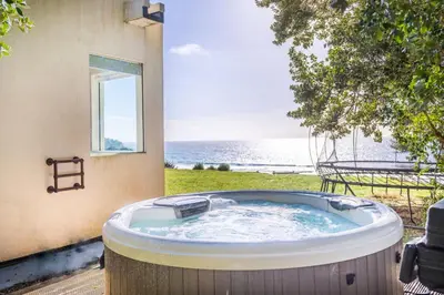 a hot tub on a patio with a view of the ocean at Footsteps from the beach - Hot tub - Cosy fireplace in Praa Sands