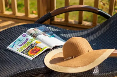 a straw hat and a book on a wicker chair at Trewhiddle Retreat V4 by Together Travel - Luxury 4-Bedroom Villa in St Austell