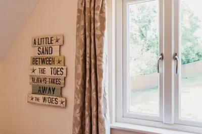 a window with a curtain and a sign that reads a little sand servedserved at Trewhiddle Retreat V31 by Together Travel - Luxury 3-Bedroom Villa in St Austell