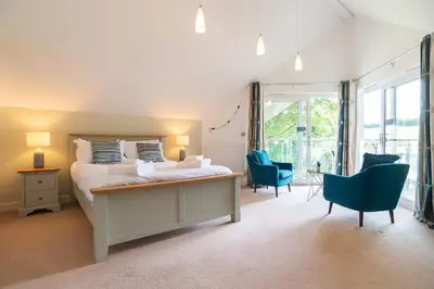 a bedroom with a bed and chairs and a large window at Trewhiddle Retreat V25 by Together Travel - Luxury 4-Bedroom Villa in St Austell