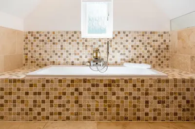 a bath tub in a bathroom with brown tiles at Trewhiddle Retreat V24 by Together Travel - Luxury 4-Bedroom Villa in St Austell