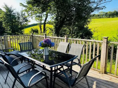 a table with chairs and a vase of flowers on a deck at Trewhiddle Retreat V20 by Together Travel - Luxury 3-Bedroom Villa in St Austell