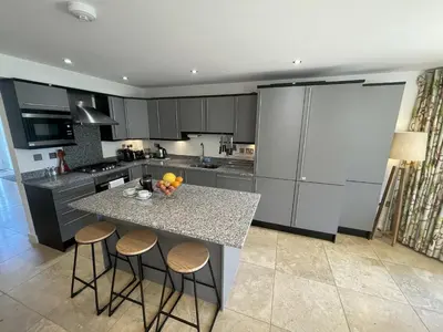 a kitchen with a island with stools and a counter top at Trewhiddle Retreat V12 by Together Travel - Luxury 4-Bedroom Villa in St Austell