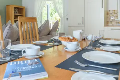 a dining room table with white plates and a book at Trewhiddle 41 by Together Travel - Stylish Coastal Countryside Retreat in St Austell