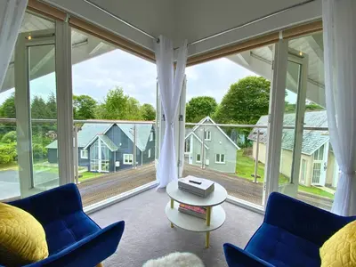 a room with a large window with blue chairs and a table at Trewhiddle Retreat V30 by Together Travel - Luxury 4-Bedroom Villa in St Austell