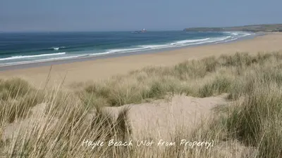 a sandy beach with grass and the ocean at 15 Tudor Court, Tolroy Manor in Hayle