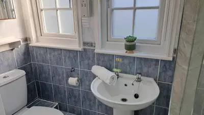 a bathroom with a sink and a toilet and windows at 28 Tudor Court, Tolroy Manor in Hayle
