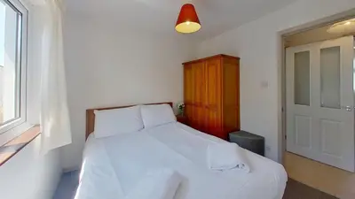a bedroom with a white bed with a wooden cabinet at D01 Vale Vue D1, Riviere Towans in Hayle
