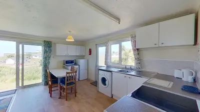 a kitchen with white cabinets and a table and a sink at D01 Vale Vue D1, Riviere Towans in Hayle
