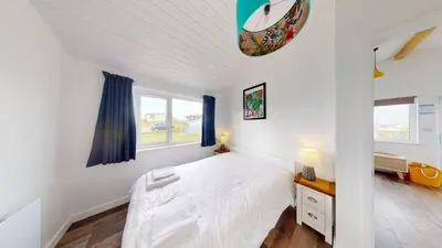 a white bedroom with a bed and two windows at D38 Miramar, Riviere Towans in Hayle