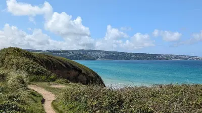 a path on a hill next to a body of water at D52 Boston, Riviere Towans in Hayle