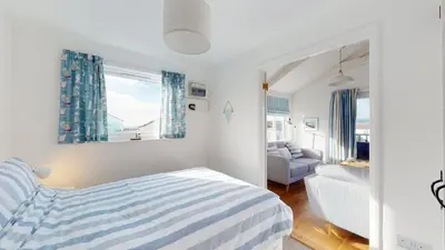 a bedroom with a striped bed and a living room at D22 Sandelite, Riviere Towans in Hayle