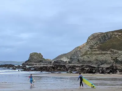 two people walking on the beach with their surfboards at No.7 Perran View in St. Agnes