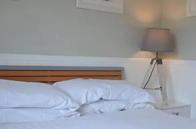 a bed with white sheets and a lamp on a table at E46 Dunroven, Riviere Towans in Hayle