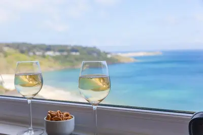 two glasses of wine and a bowl of pretzels in front of a window at Dolphin Watch in Carbis Bay