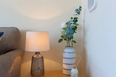 a table with a lamp and a vase with flowers at Dolphin Watch in Carbis Bay
