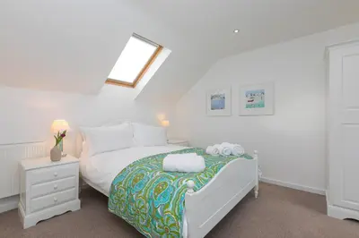 a white bedroom with a bed and a night stand at Chy Lowen in Carbis Bay