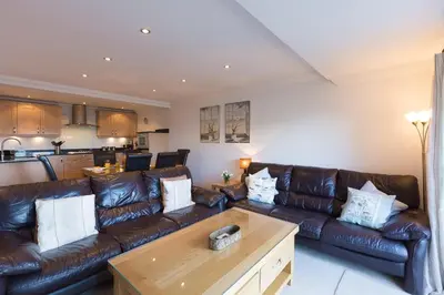 a living room with brown leather couches and a table at Gennaker in Carbis Bay